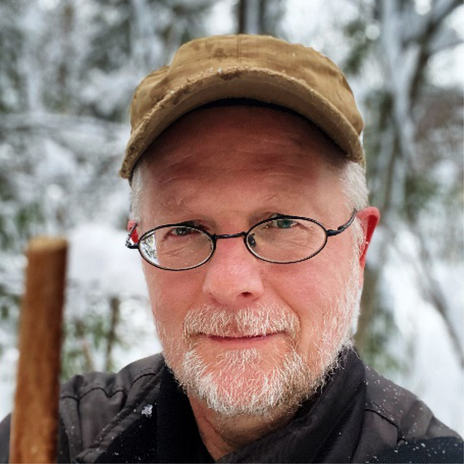 Porträttfoto av man i glasögon och skärmmössa som står i snöig skog.
