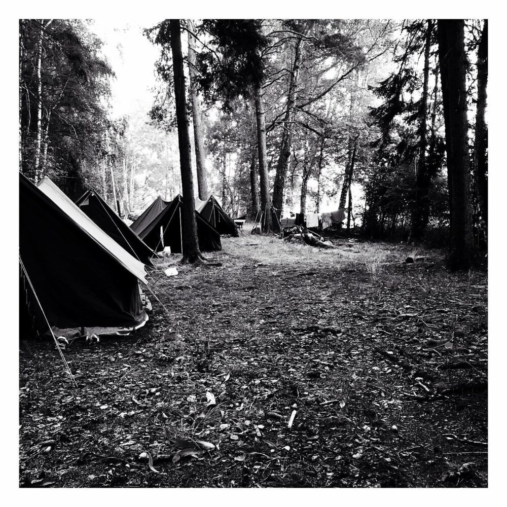 Svartvitt foto på tält i en skogsglänta.