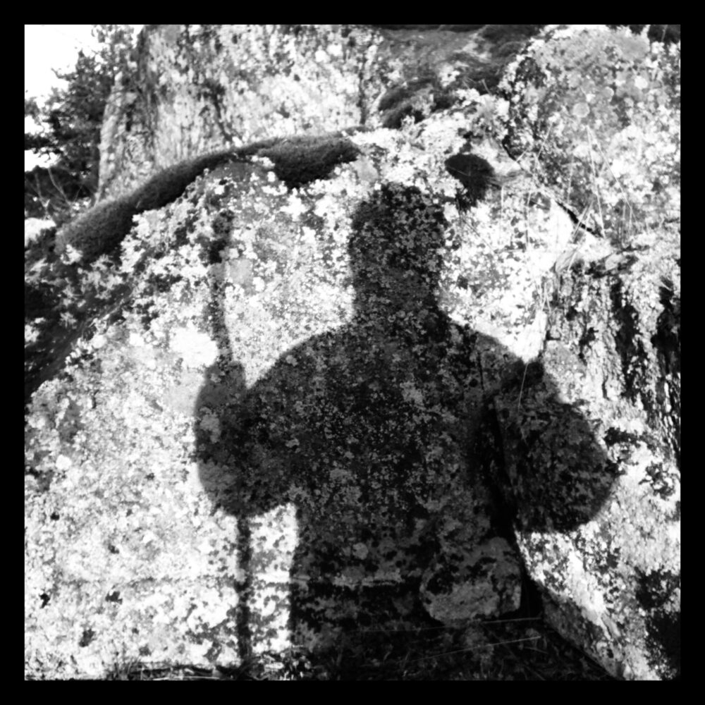 Svartvitt foto, skuggan av en person som håller en stav faller på en klippvägg.