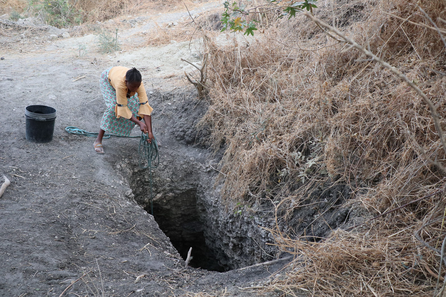 Kvinna hissar upp vatten ur en grop i marken.